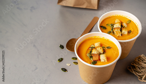 Thick vegan pumpkin cream soup with seeds and croutons in disposable cups of craft paper. Soup to go. Healthy food delivery. Space for text