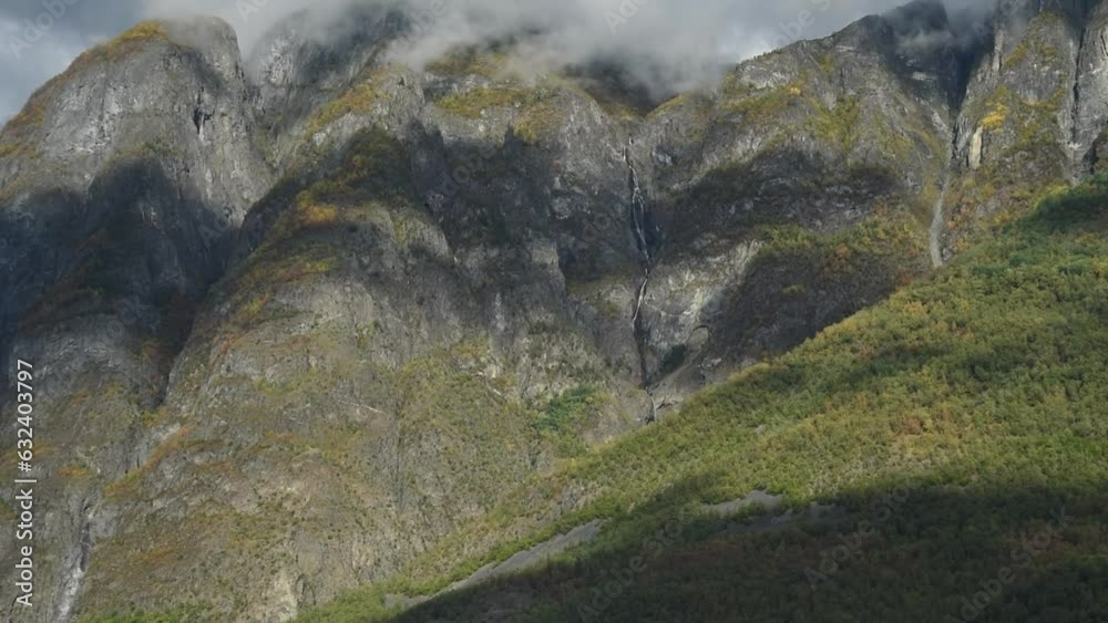 Close up view of a steep mountain slope with a autumn forest and waterfalls. Impressive timeless landscape of Norway Close up view of a steep mountain slope with a autumn forest and waterfalls. Impressive timeless landscape of Norway