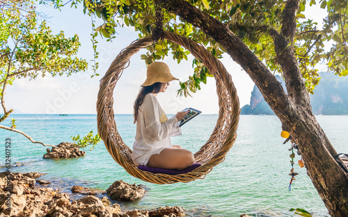 Sticker Traveler woman relaxing on straw nests using tablet at Railay beach Krabi, Asia