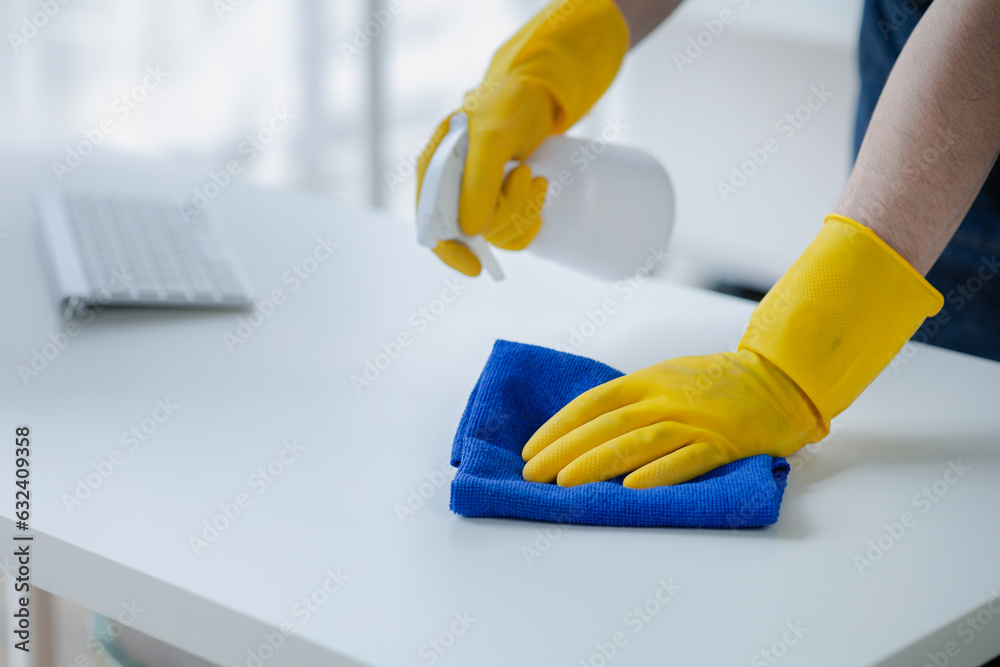 Person cleaning the room, cleaning staff is using cloth and spraying disinfectant to wipe the tables in the company office room. Cleaning staff. Maintaining cleanliness in the organization.