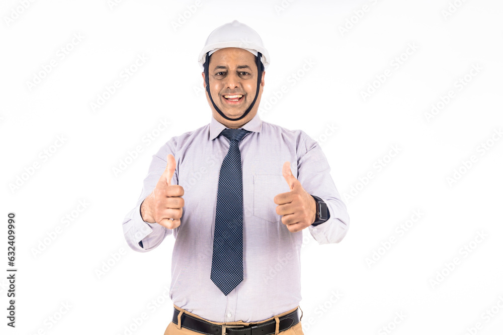 Young Indian engineer wearing hard hat and showing thumps up on white background.
