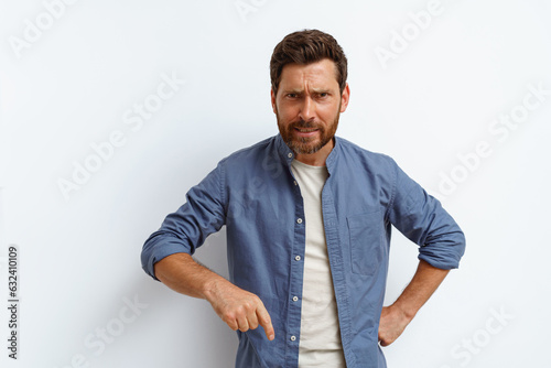 Angry man points finger down and say to you come here right now while standing on white background