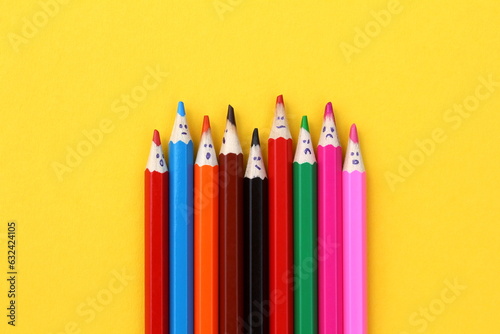 Multi-colored pencils with painted faces lie on a yellow background.