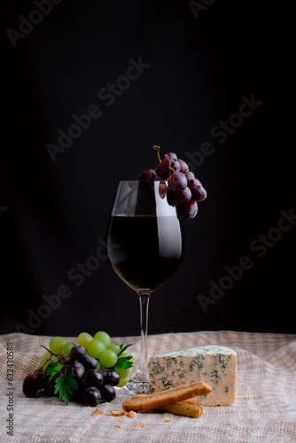 A wine glass with red wine and a bunch of grape