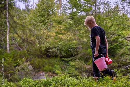 A young boy is in a forest picking bluberries with a berry picker