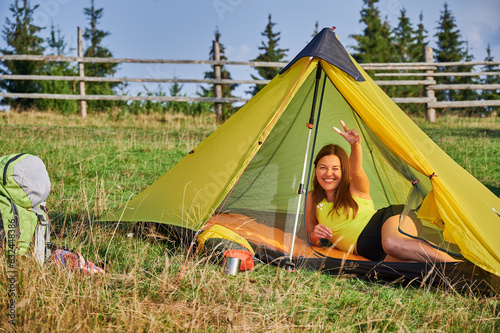 Woman hiker camping outdoors. Attractive, sporty tourist traveling in summer. Beautiful, young female lying in tent, having break, looking at camera. Concept of tourism and hiking.