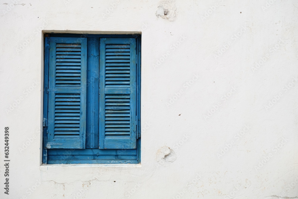 Blue window with wooden shutters on a white stone wall