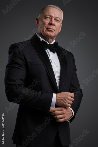 Сonfident and stylish mature man with grey hair dressed in a stylish black suit and bowtie