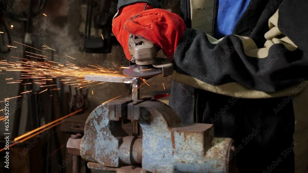 Close-up of a blacksmith man working with a metal grinder in a forge. A lot of sparks are flying around. Cutting metal angle grinder. Sawing metal.