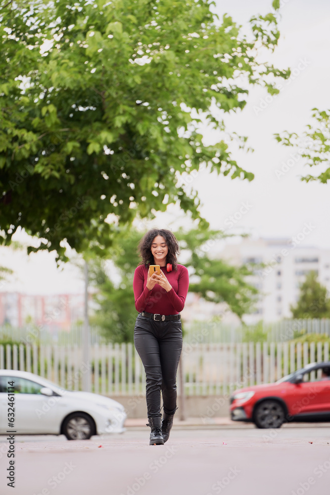 Woman smiling while using her mobile phone walking outdoors. Technology concept. Woman smiling while using her mobile phone walking outdoors. Technology concept.