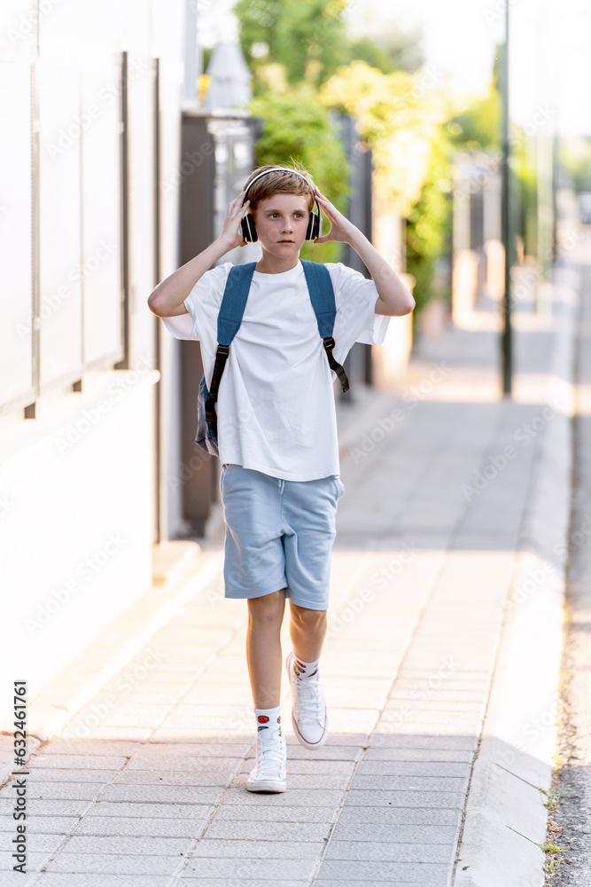 Teenage boy with backpack listening to music with headphones while walking down the street.