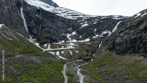 Trollstigen mountain pass days before opening with snow left in terrain - Aerial approaching hillside above closed road photo