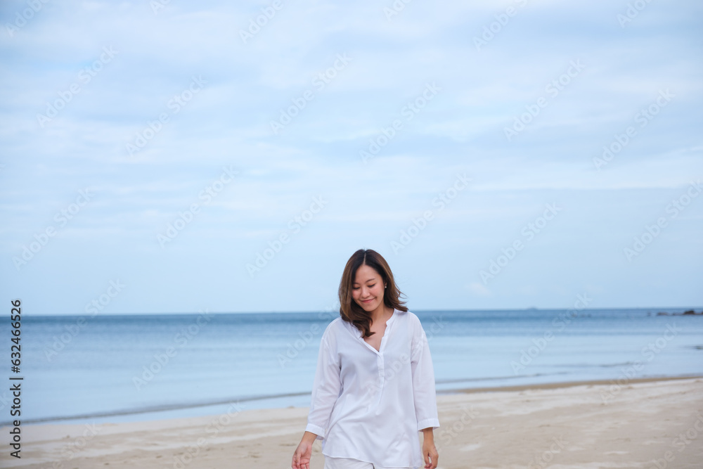 Portrait image of a beautiful young asian woman while strolling on the beach with the sea and blue sky Portrait image of a beautiful young asian woman while strolling on the beach with the sea and blue sky