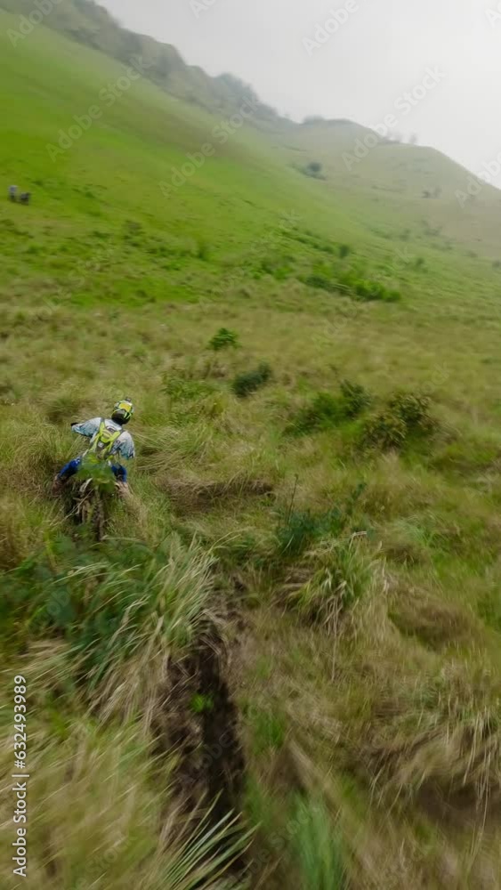 Vertical video. Fpv drone aerial flying over enduro motorcyclists riding downhill green mountains. Group bikers waiting resting of the hill. Cross country extremal moto riders sporty trying move down Vertical video. Fpv drone aerial flying over enduro motorcyclists riding downhill green mountains. Group bikers waiting resting of the hill. Cross country extremal moto riders sporty trying move down