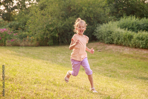 Happy girl jumping and running on the green lawn, schoolchildren summer vacation, fun and outdoor games. 
