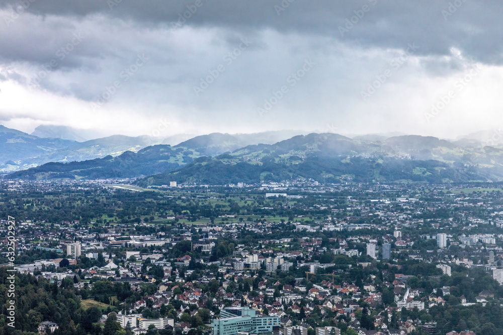 Fototapeta premium View at Bregenz and surrounding towns and mountains from mount Pfänder, a local mountain in austria at a rainy day in summer