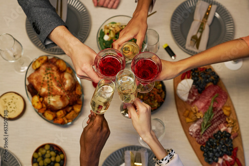 Top view of hands of young intercultural friends with alcoholic drinks clinking with flutes and wineglasses over table served for dinner