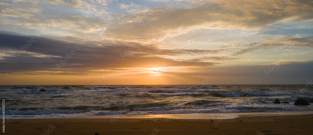Sunset over ocean waves wash sand beach panorama