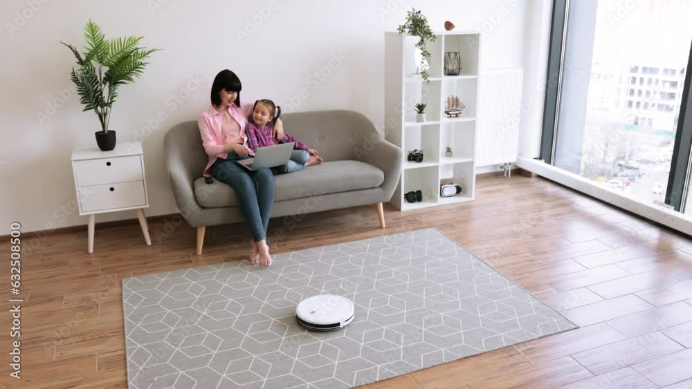 Young caucasian female with tween child using remote control for smart cleaning device in living room of apartment. Mom and daughter doing household chores with electronic device saving time for fun. Young caucasian female with tween child using remote control for smart cleaning device in living room of apartment. Mom and daughter doing household chores with electronic device saving time for fun.