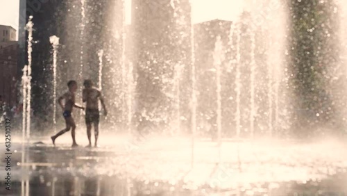 Children splashing in a city fountains on a hot summer evening. Unfocused or blurred view background, slow motion, 4K footage
