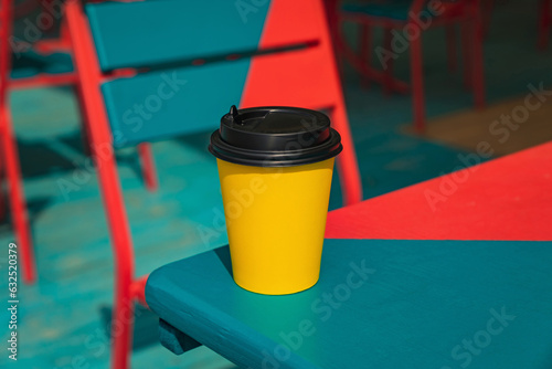 Bright yellow takeaway coffee cup on a colourful wooden table