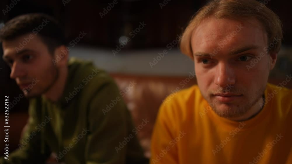 Positive man yelling in slow motion watching TV with blurred friend at background. Happy Caucasian carefree relaxed friends cheering enjoying leisure on weekend indoors Positive man yelling in slow motion watching TV with blurred friend at background. Happy Caucasian carefree relaxed friends cheering enjoying leisure on weekend indoors
