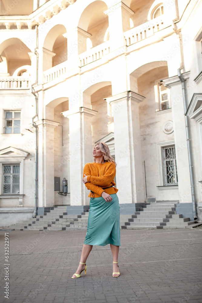 A beautiful  girl walks through the streets of the cityю The woman is wearing fashion clothes, green skirt and yellow sweater