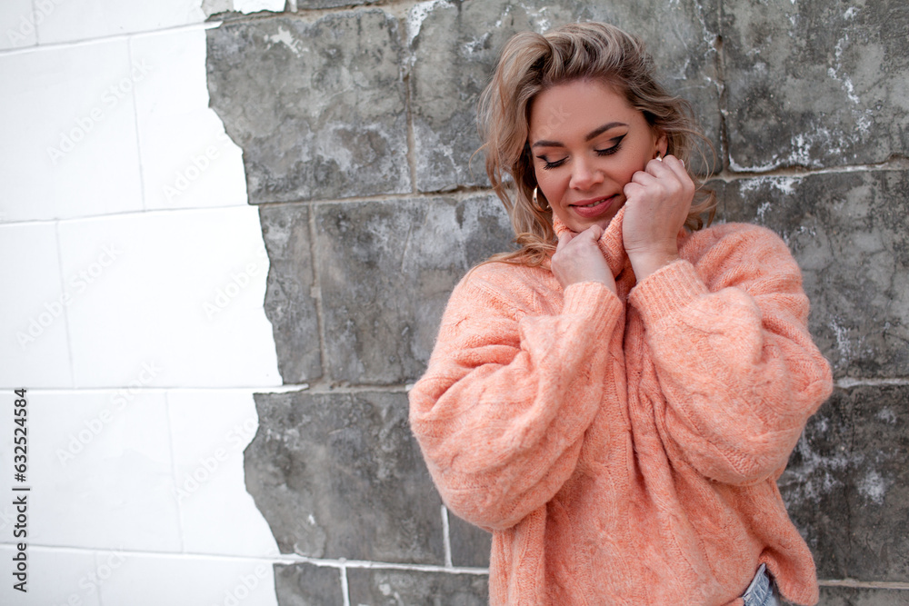 Stylish girl with blomd hair wearing a peach sweater walks in the ...