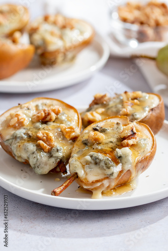 Baked pears with blue cheese, walnuts and honey on white plate and light background