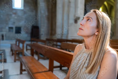 A woman is facing the altar praying while sitting on a wooden pew in a church.