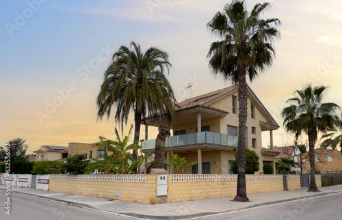 Villa with Garden. Fence at a suburb house. Design house and luxury facilities. Garden Home building Exterior. Luxury Villa with palm trees in garden. Gate and brick wall of fence on street sidewalk. © MaxSafaniuk