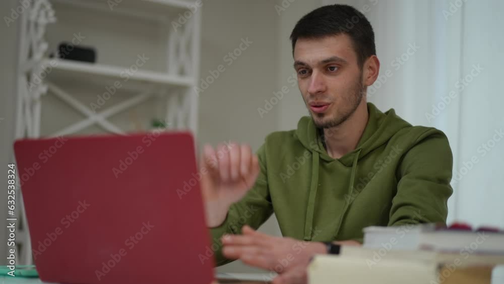 Portrait of positive confident man waving greeting in video chat on laptop sitting in home office. Smiling Caucasian freelancer working remotely talking in slow motion