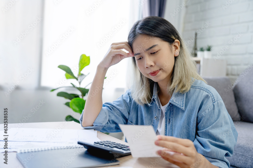 Strain face Asian woman hand holding expense bill and calculation about debt bills monthly at the table in home Strain face Asian woman hand holding expense bill and calculation about debt bills monthly at the table in home