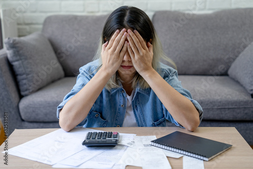 Canvas Print Asian woman sitting covering face with hands with many bills on table at home