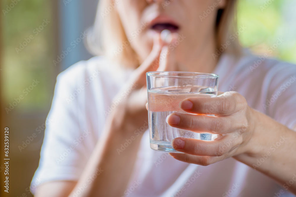 in the woman's hand, a glass of water washes down a tablet with water in the woman's hand, a glass of water washes down a tablet with water
