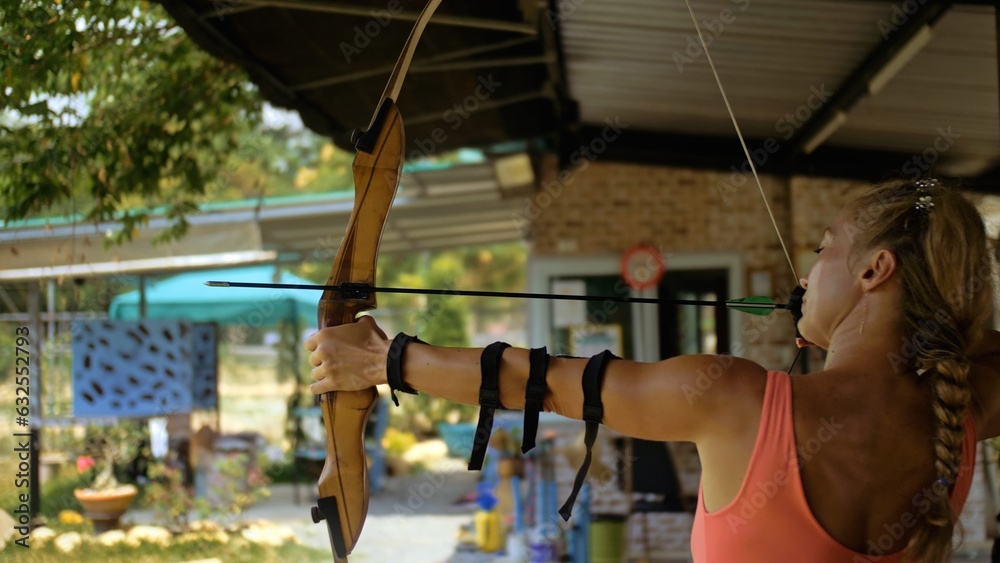 Sport woman in shooting range with bow. Sportsman in shooting gallery aim an arrow to hit target. Outdoor archery training. Practice and training of archery in shooting range. Athlete keep wooden bow Sport woman in shooting range with bow. Sportsman in shooting gallery aim an arrow to hit target. Outdoor archery training. Practice and training of archery in shooting range. Athlete keep wooden bow