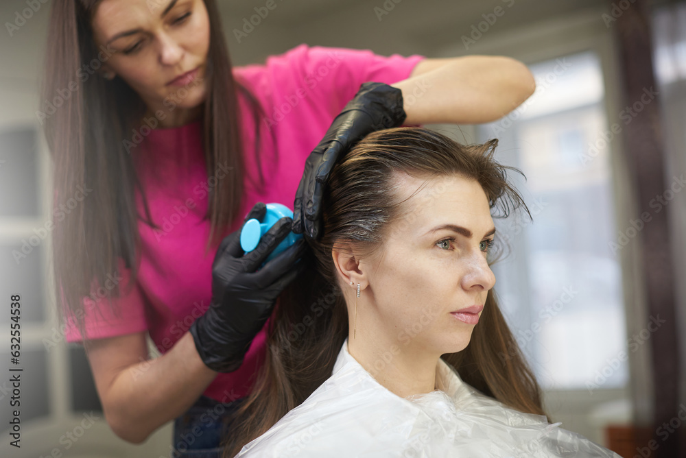 Naklejka premium The hair stylist applies hair mask for keratin straightening procedure