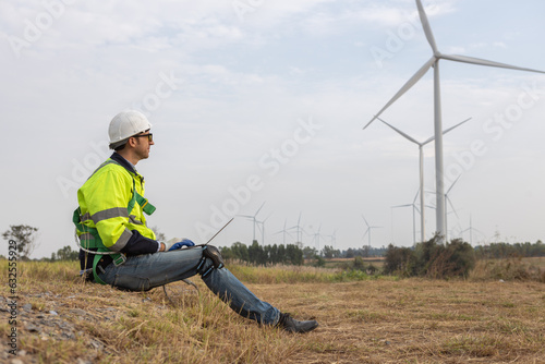 Wind turbine technician using laptop checking and maintenance at turbine station. Man engineer working at energy wind generator. clean energy source.
