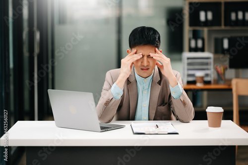 Frustrated young businessman working on a laptop computer sitting at his working place in office.