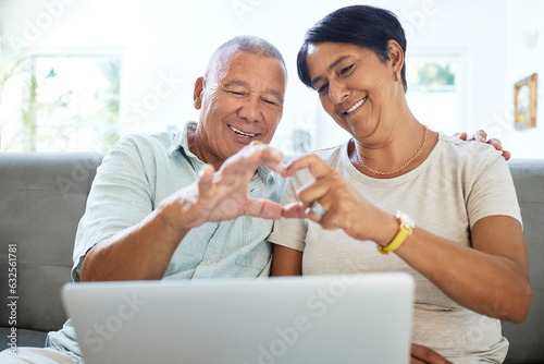 Mature couple, heart hands and laptop on home sofa for video call, streaming and internet. A happy man and woman together on a couch with technology for communication, social media emoji or love