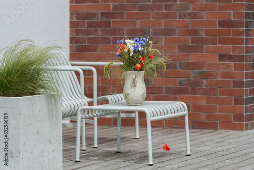 Wild flower bouquet (Cornflowers, chamomiles wheat and poppies) in terracotta vase on summer terrace. Wildflower and grass varieties.