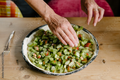 Unrecognizable man baker standing near table and arranging cut green rhubarb pieces on pie dough