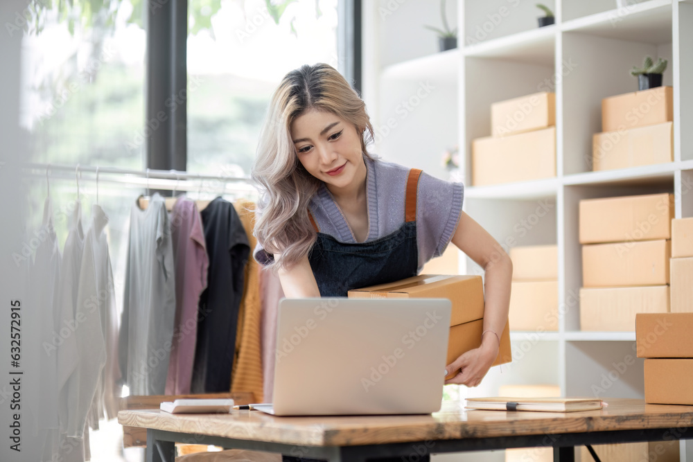 Portrait of a Asian start-up business owner, looking at camera, working happily with cardboard boxes at home, preparing to ship clothes in sme Portrait of a Asian start-up business owner, looking at camera, working happily with cardboard boxes at home, preparing to ship clothes in sme