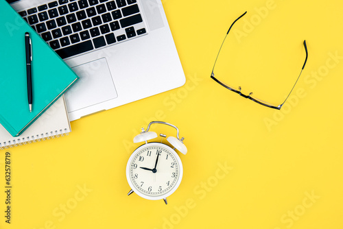 Laptop, alarm clock and glasses on a yellow background.