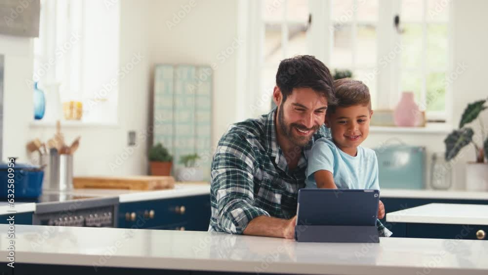 Father at home in kitchen with son streaming or playing game on digital tablet - shot in slow motion Father at home in kitchen with son streaming or playing game on digital tablet - shot in slow motion
