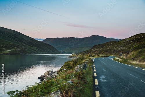 Connemara loop or road as the sun sets on Killary Fjord, Connemara National Park. Western Ireland sunset as the scenic N59 route stretches beside the calm ocean water surrounded by mountains. Ireland photo