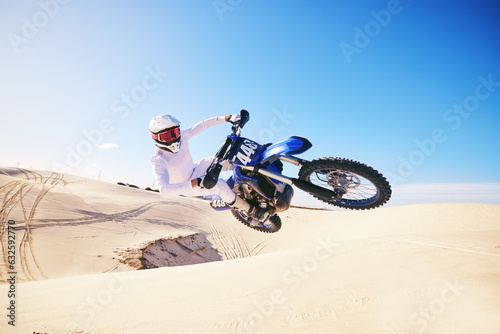 Sand, motor sports and man in air with motorbike for adrenaline, adventure and freedom in desert. Action, extreme sport and male person on bike on dunes for training, exercise and race or challenge photo