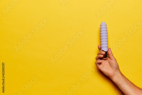 Female hand with vibrator, medical massager over bright yellow background. Image for sex shop. Concept of health, medicine, ad