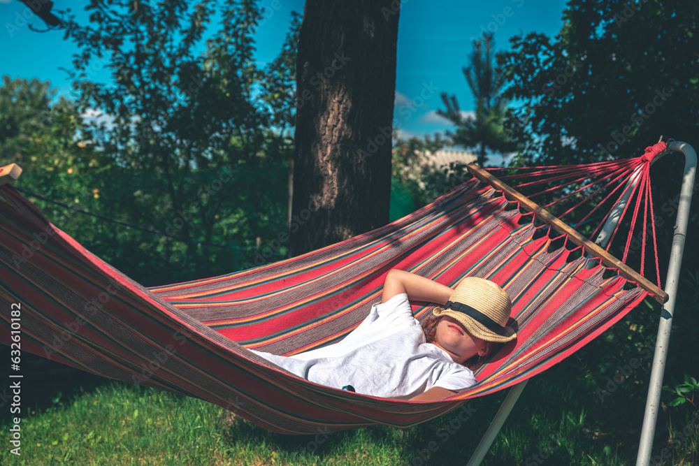 The girl lies on a hammock, covering her face with a hat