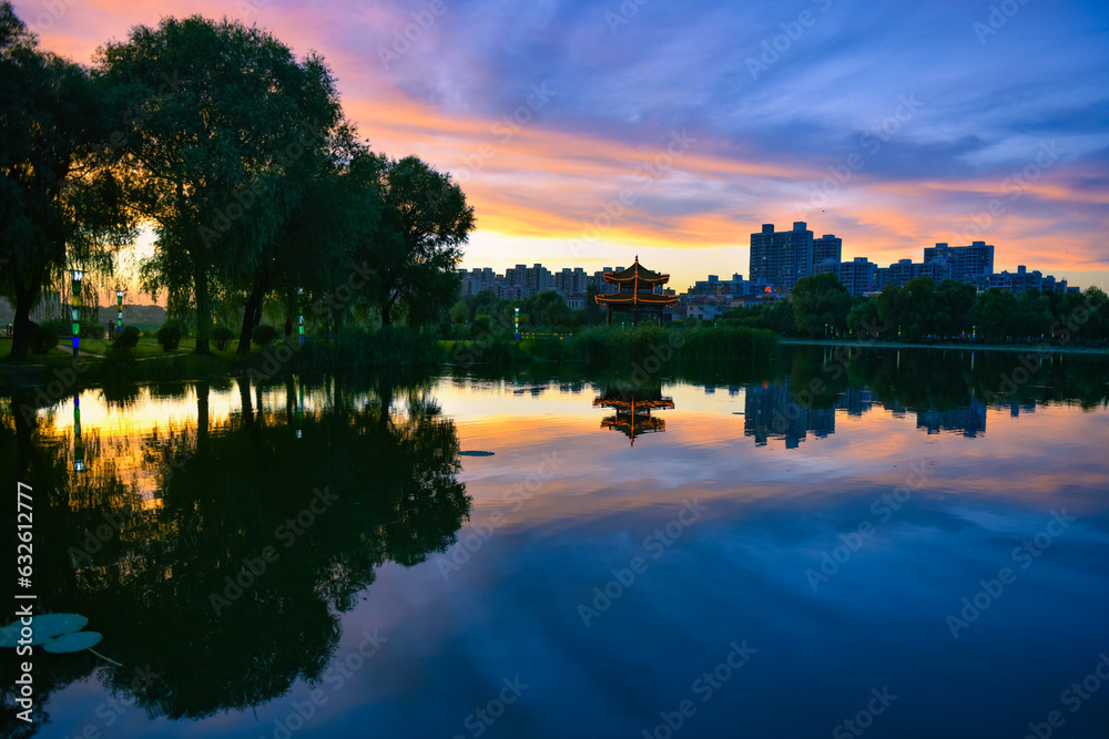 In the city park, the beautiful sunset reflects the cloudy sky and the river surface of the lotus pond